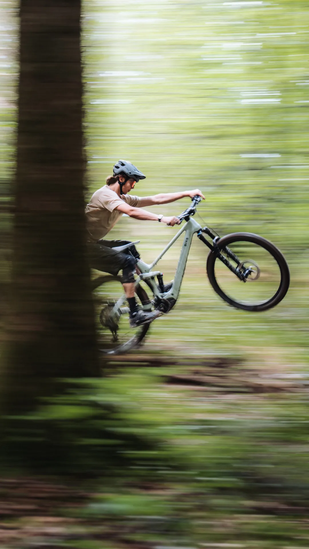 Mountainbiker springt mit BIXS Fully-Mountainbike über einen Waldtrail, Bewegungsunschärfe