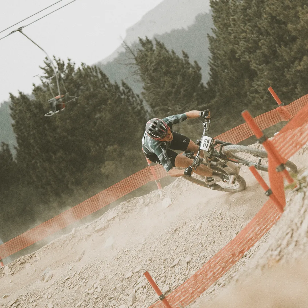 BIXS-Mountainbiker mit Startnummer 22 in staubiger Steilkurve, Bergkulisse im Hintergrund