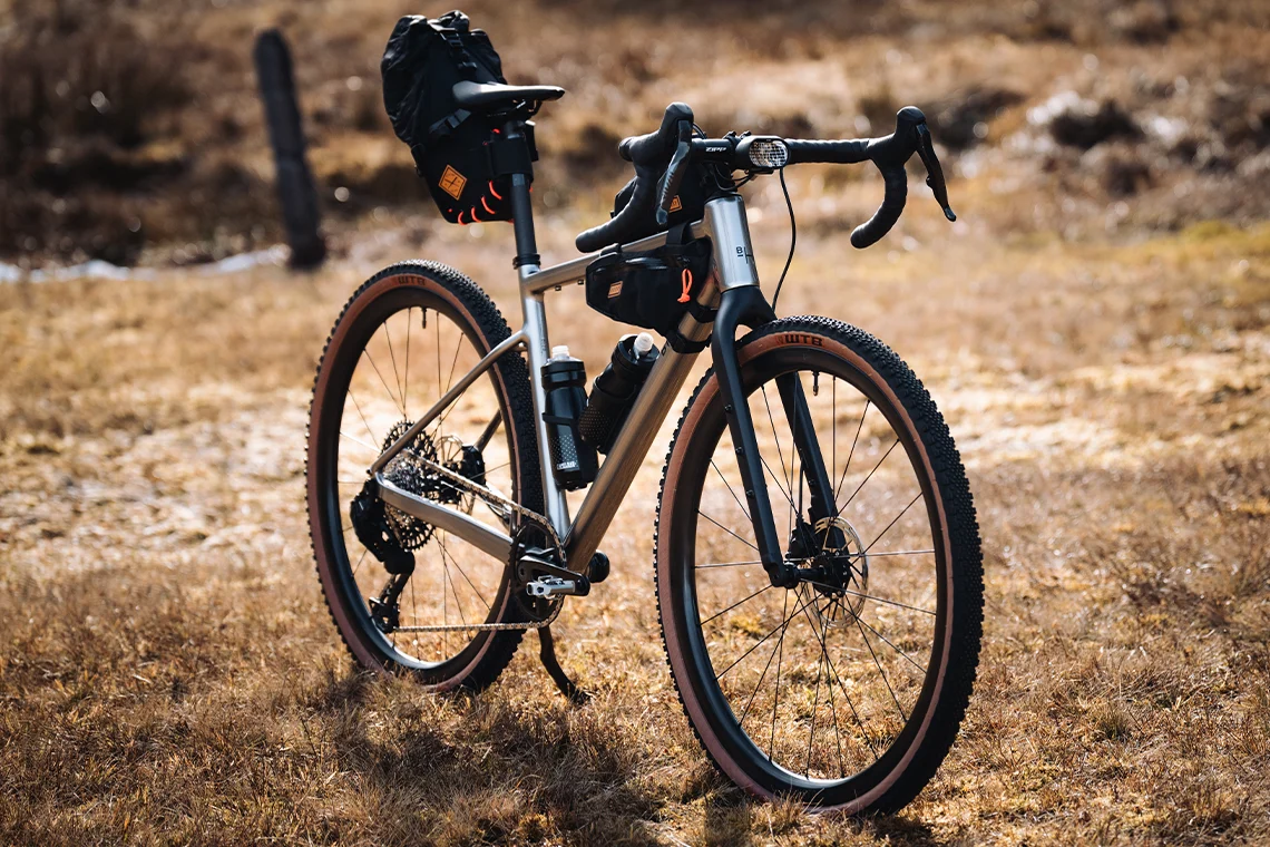 Ein Gravelbike mit dicken Reifen und mehreren Fahrradtaschen steht auf einer Wiese unter strahlend blauem Himmel.