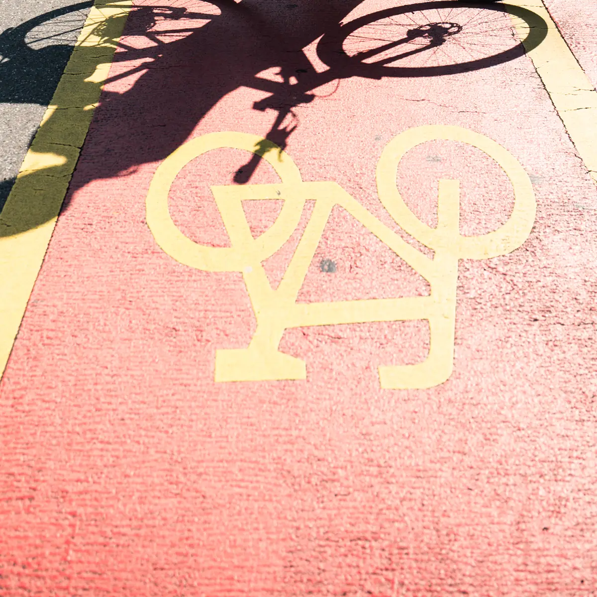 Schatten eines Fahrrads über einem gelben Velo-Piktogramm auf rotem Fahrradweg