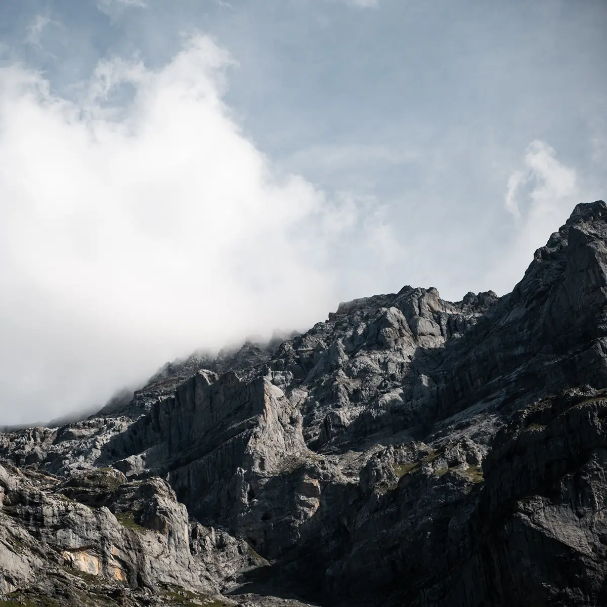Zerklüfteter Alpengipfel teilweise in Wolken gehüllt vor blauem Himmel