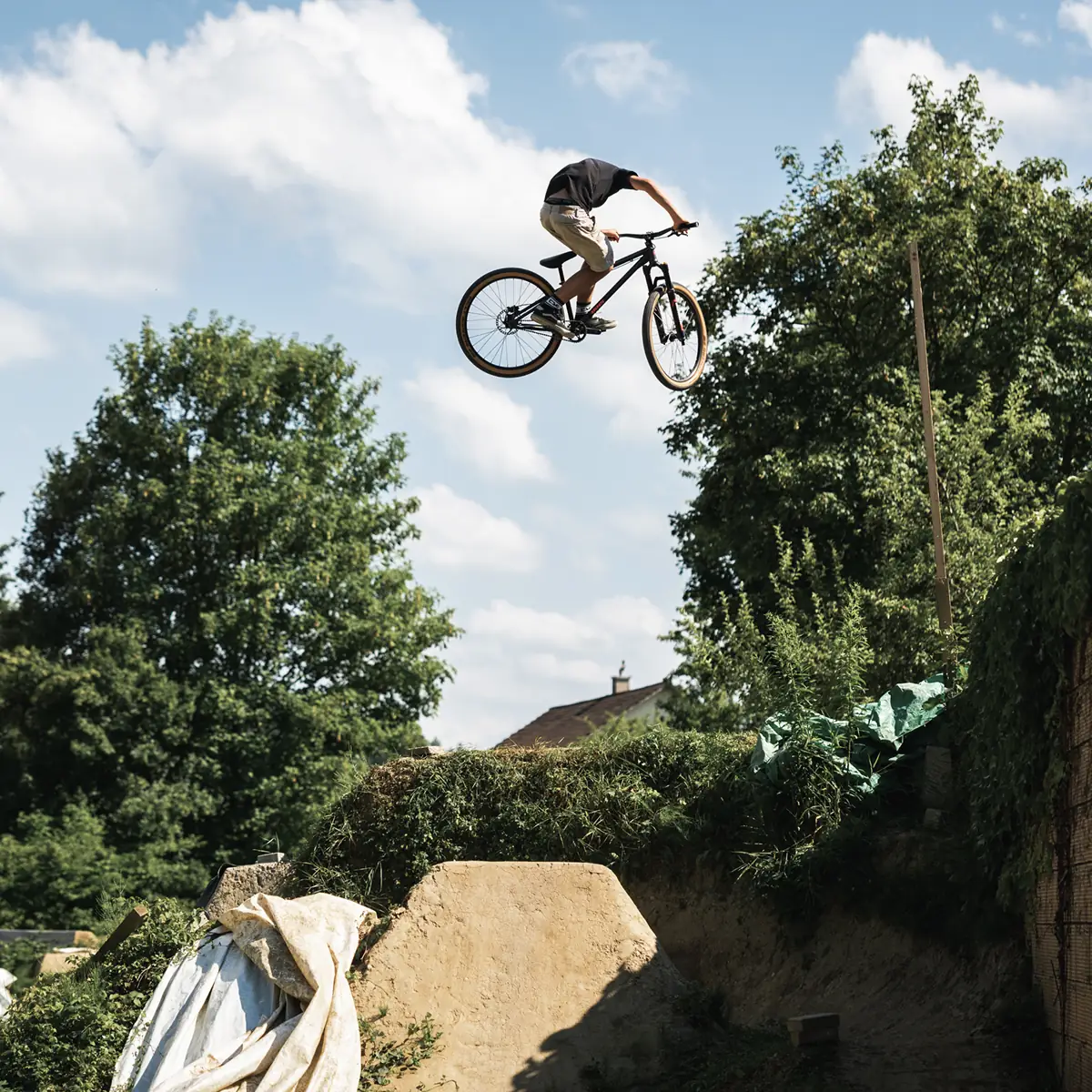 Fahrer springt mit schwarzem BIXS Dirtjump-Bike über eine Backyard-Dirtstrecke