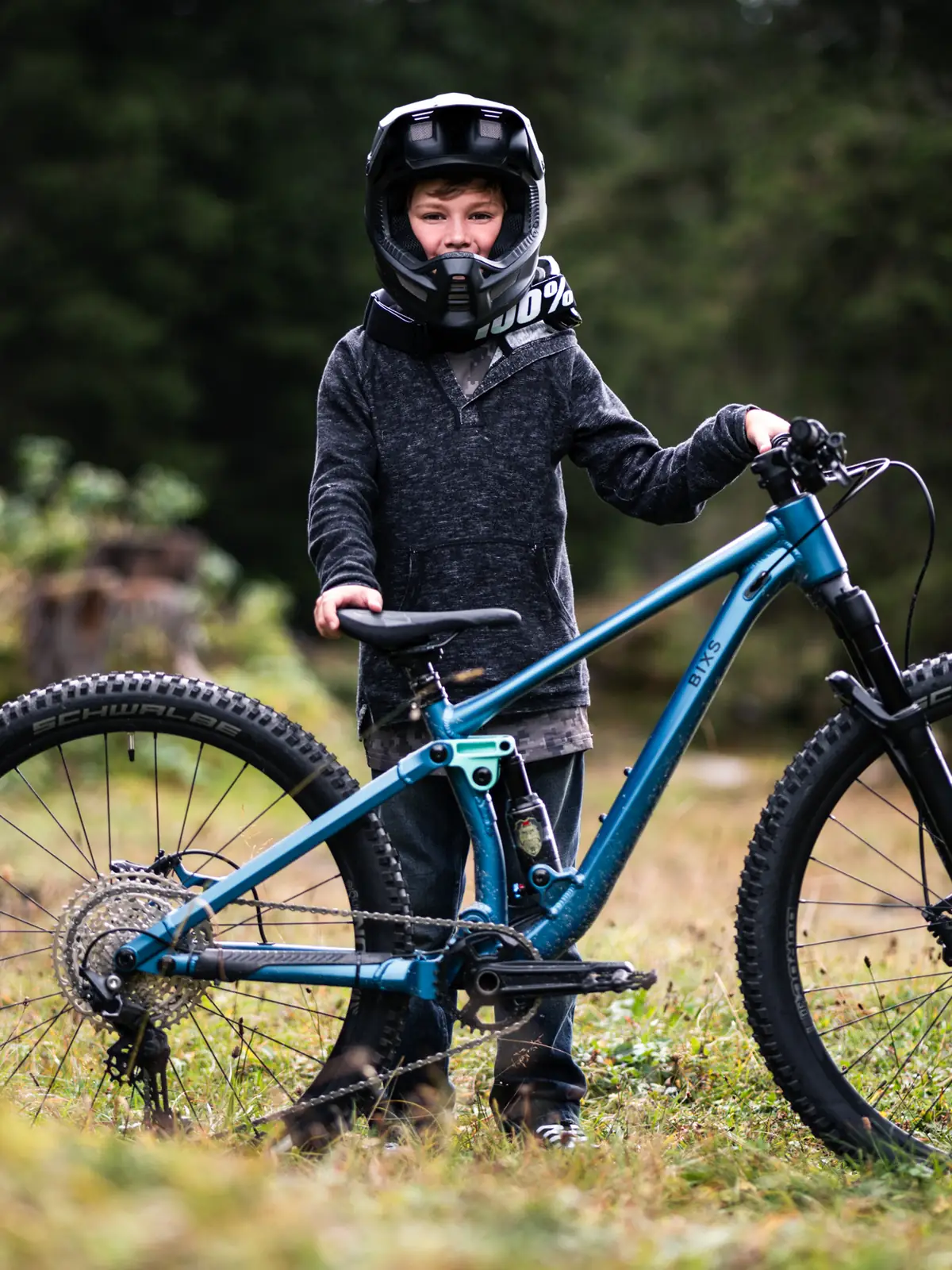 Niels mit Fullface-Helm steht neben seinem blauen BIXS Kids-Mountainbike auf einer herbstlichen Wiese