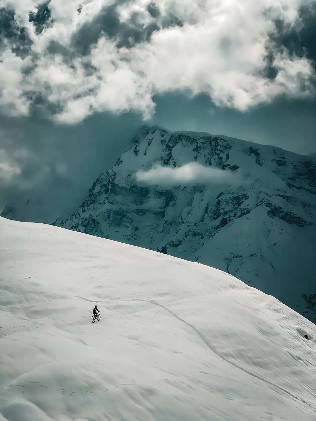 Einzelner Fahrer auf schneebedecktem Hang vor dramatischer Bergkulisse