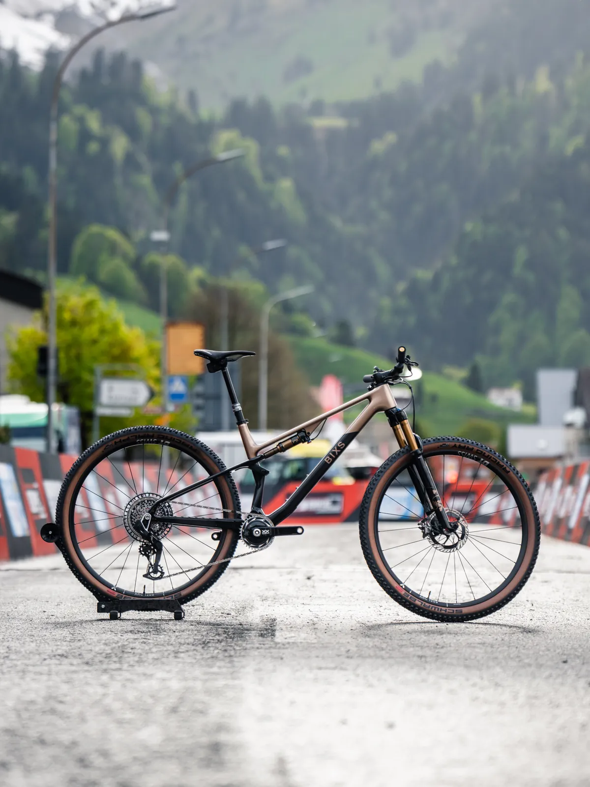 BIXS Pace Cross-Country-Bike in Bronze auf Radständer vor Absperrungen und Alpenkulisse