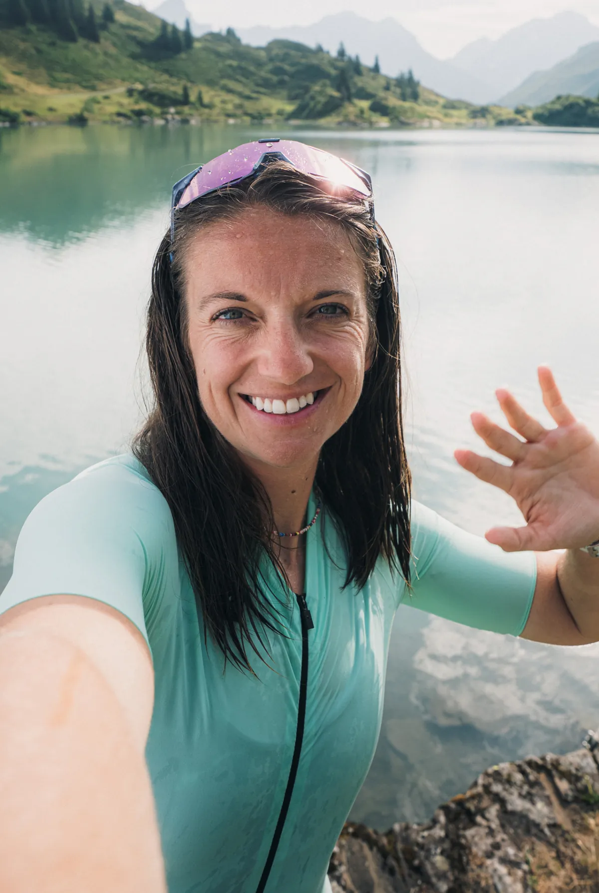 Bikerin mit nassen Haaren und Brille auf dem Kopf macht ein Selfie an einem türkisfarbenen Bergsee