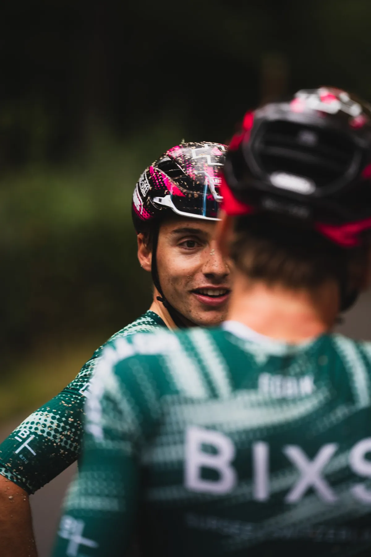 Zwei Fahrer im BIXS-Teamtrikot mit schlammbespritzten Helmen unterhalten sich nach dem Rennen