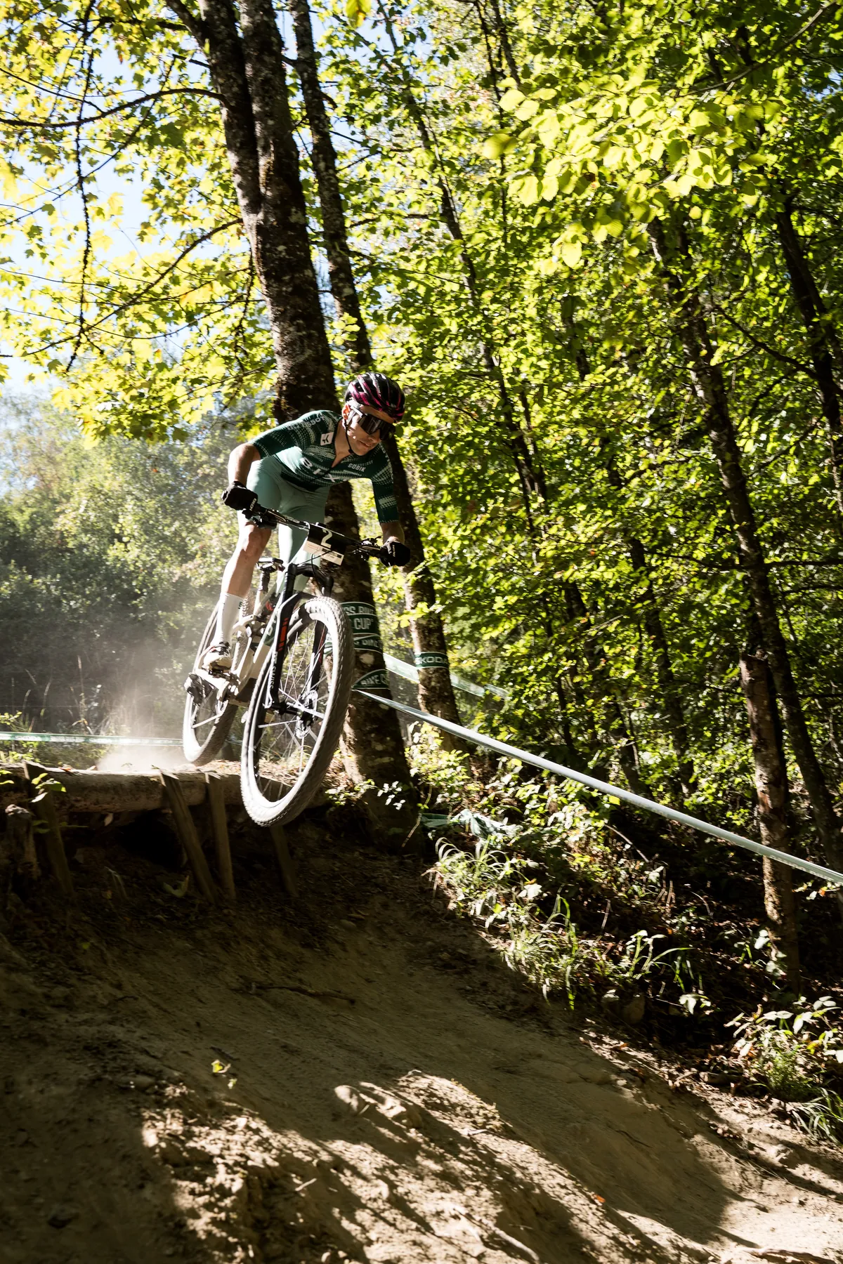 Fahrer im BIXS-Trikot springt mit seinem Cross-Country-Bike über einen Holzdrop im Wald