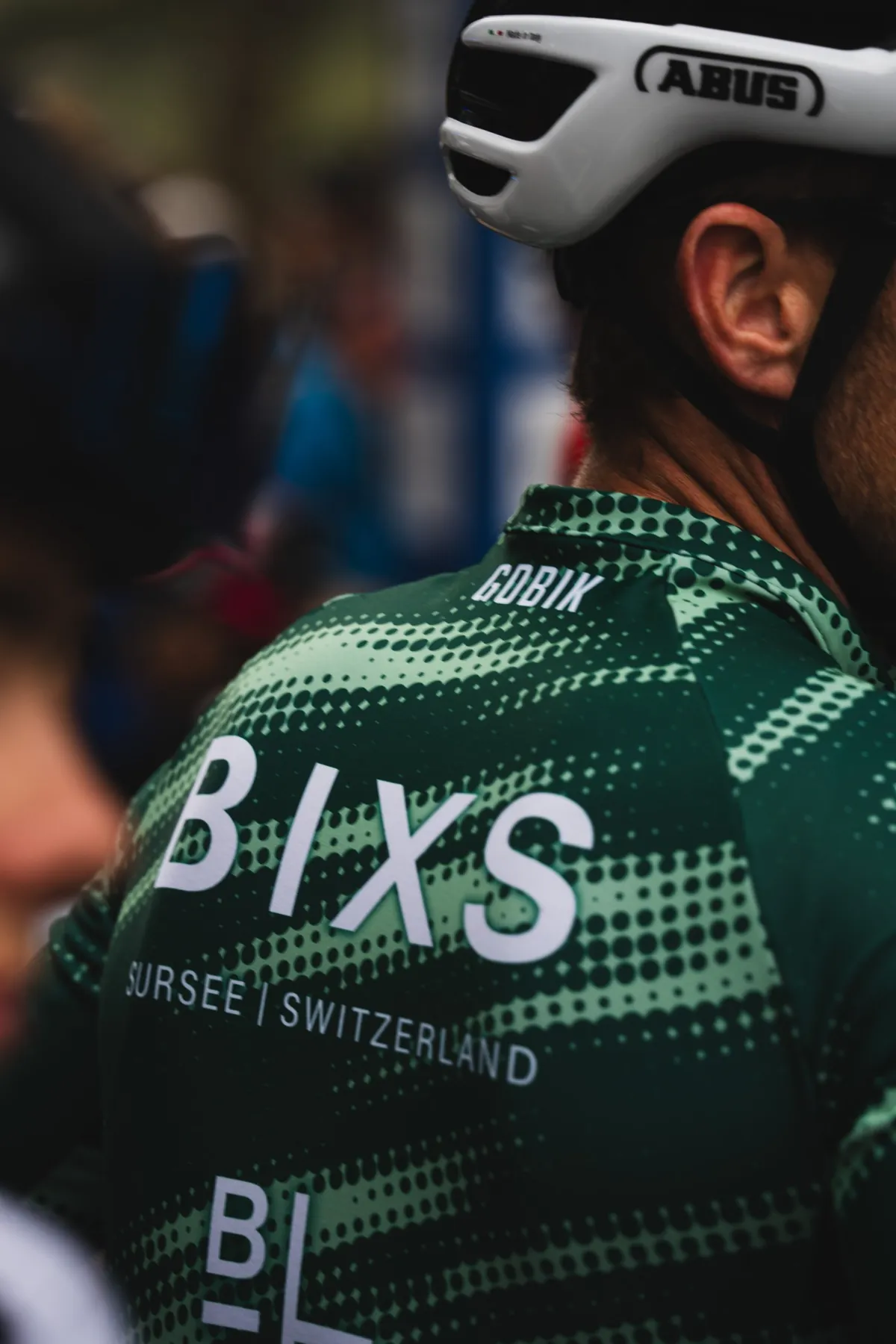 Rückenansicht eines Fahrers im grünen BIXS-Teamtrikot mit Schriftzug «BIXS Sursee Switzerland» und weissem Helm