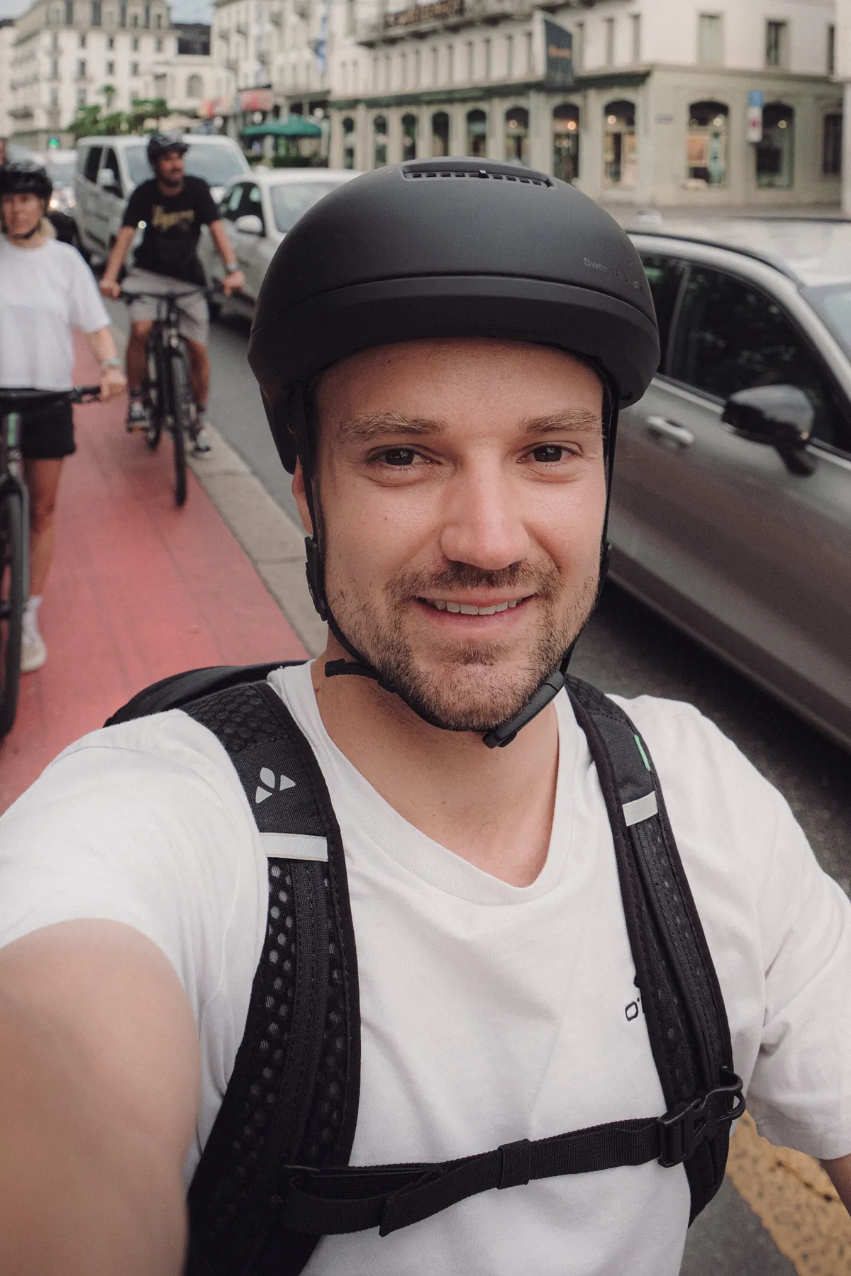 Velofahrer mit Urban-Helm und Rucksack macht ein Selfie auf einem roten Veloweg neben stehenden Autos