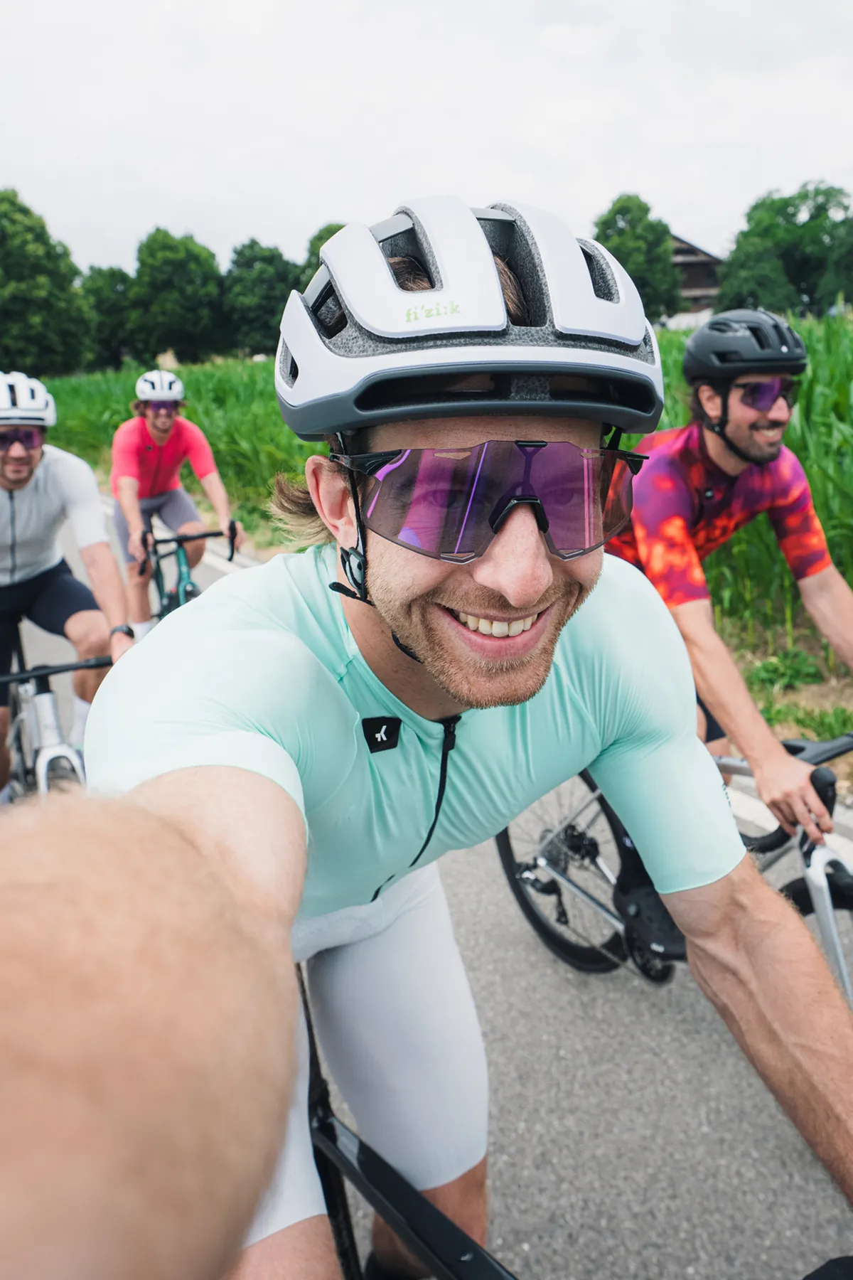 Rennradfahrer macht während der Fahrt ein Selfie, drei weitere Fahrer folgen auf der Landstrasse
