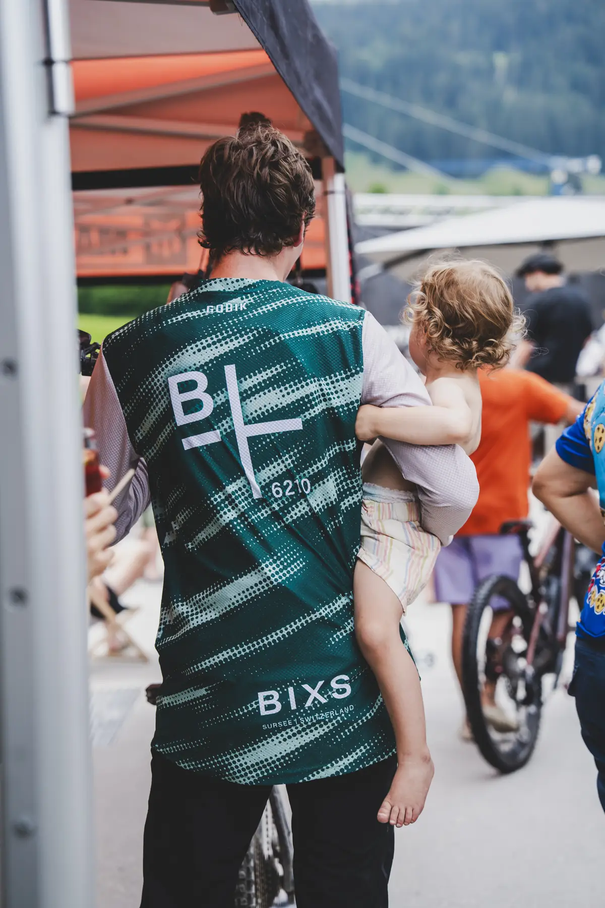 BIXS-Fahrer im Teamtrikot trägt ein Kind durchs Fahrerlager der Swiss Enduro Series in Flims
