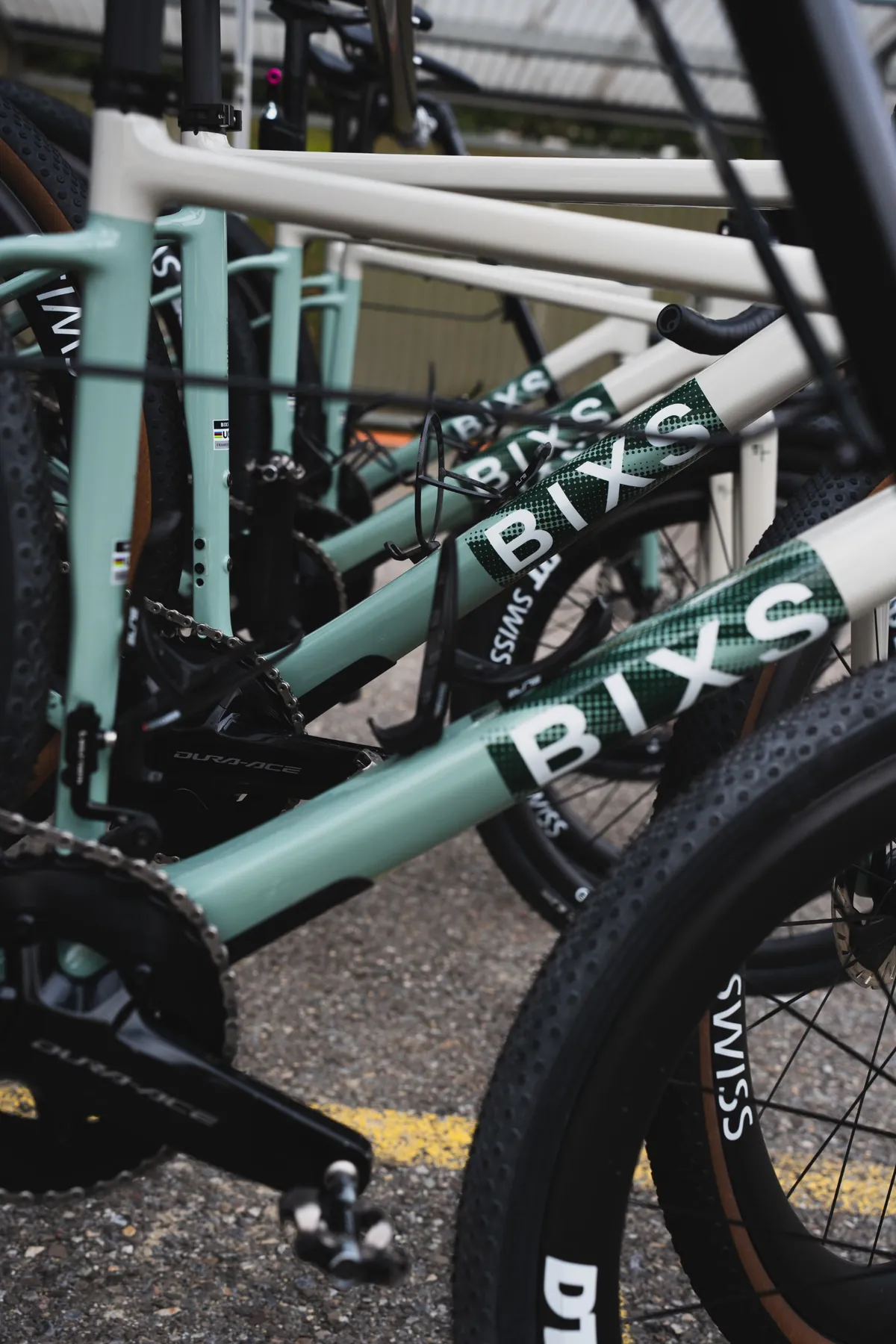 Mehrere BIXS Gravelbikes in Mint und Weiss stehen dicht nebeneinander, Oberrohre mit grossem BIXS-Schriftzug
