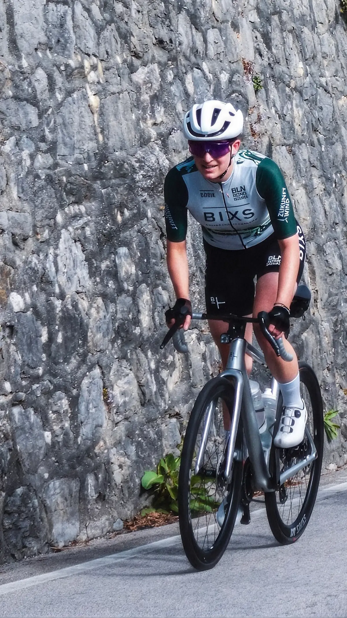 Fahrerin auf Rennrad vor Steinmauer auf kurviger Strasse