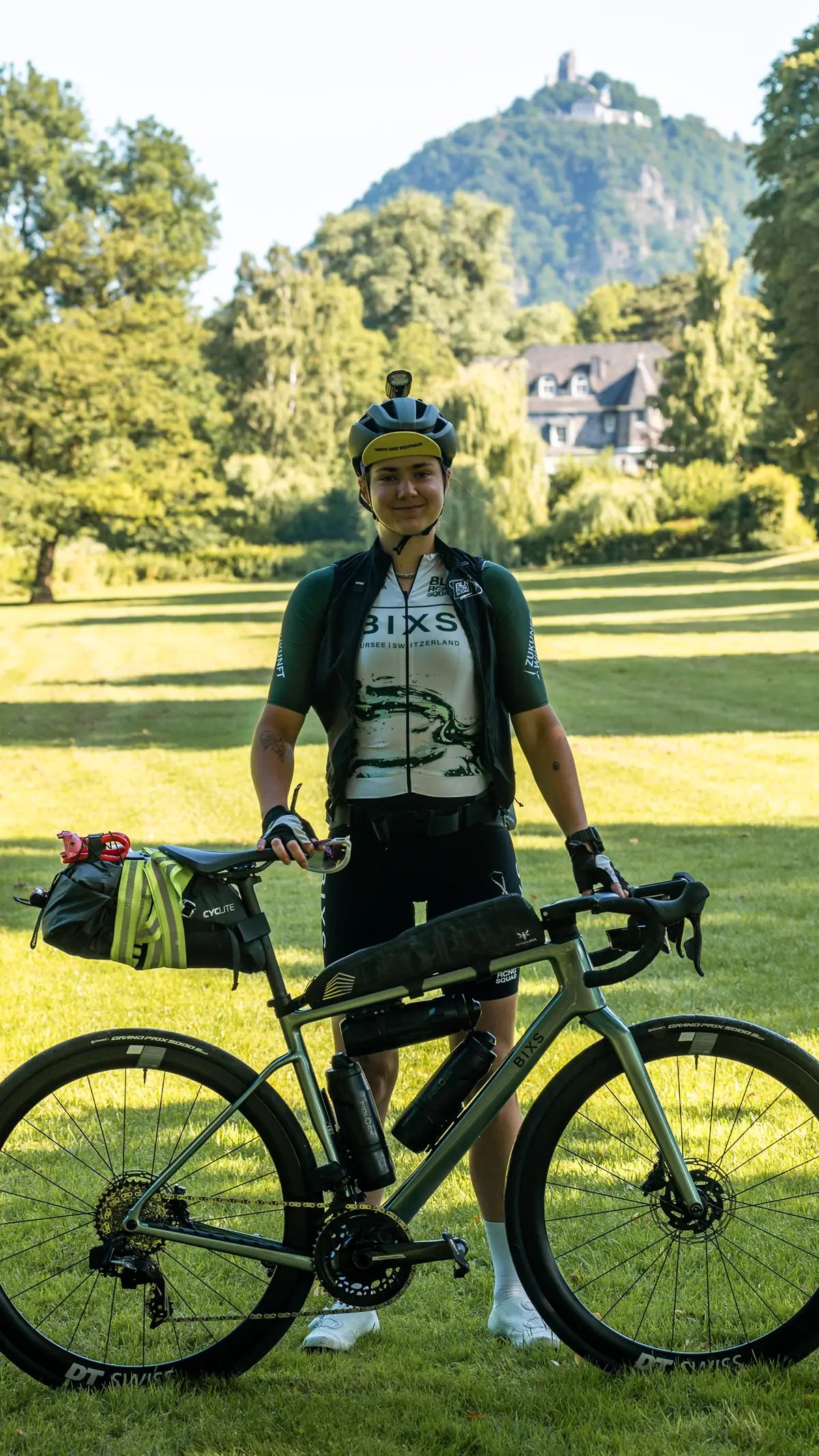 Fahrerin mit Bikepacking-Gepäck steht mit Gravelbike vor Schlosshügel