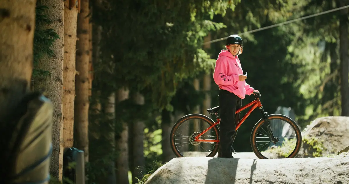 Fahrerin mit Dirtjump-Bike steht auf Felsblock im Wald