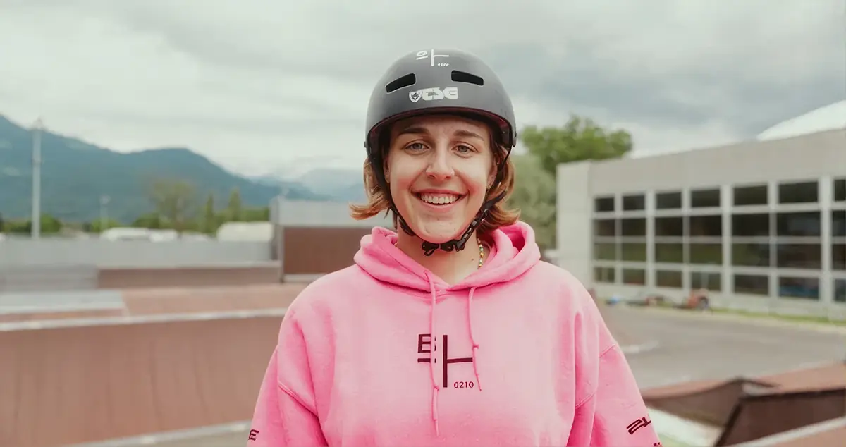 Lächelnde Fahrerin mit Helm im Skatepark, Berge im Hintergrund