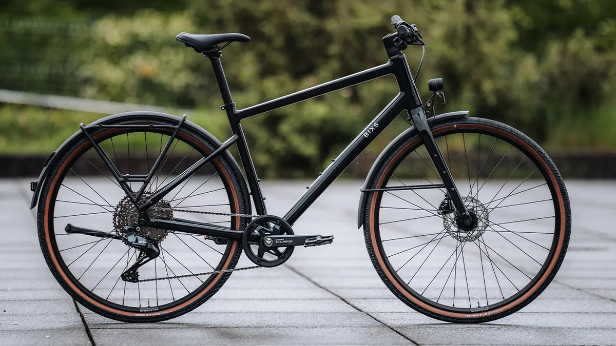 BIXS District E-Bike in Schwarz vor grüner Hecke auf regennasser Steinplattenterrasse