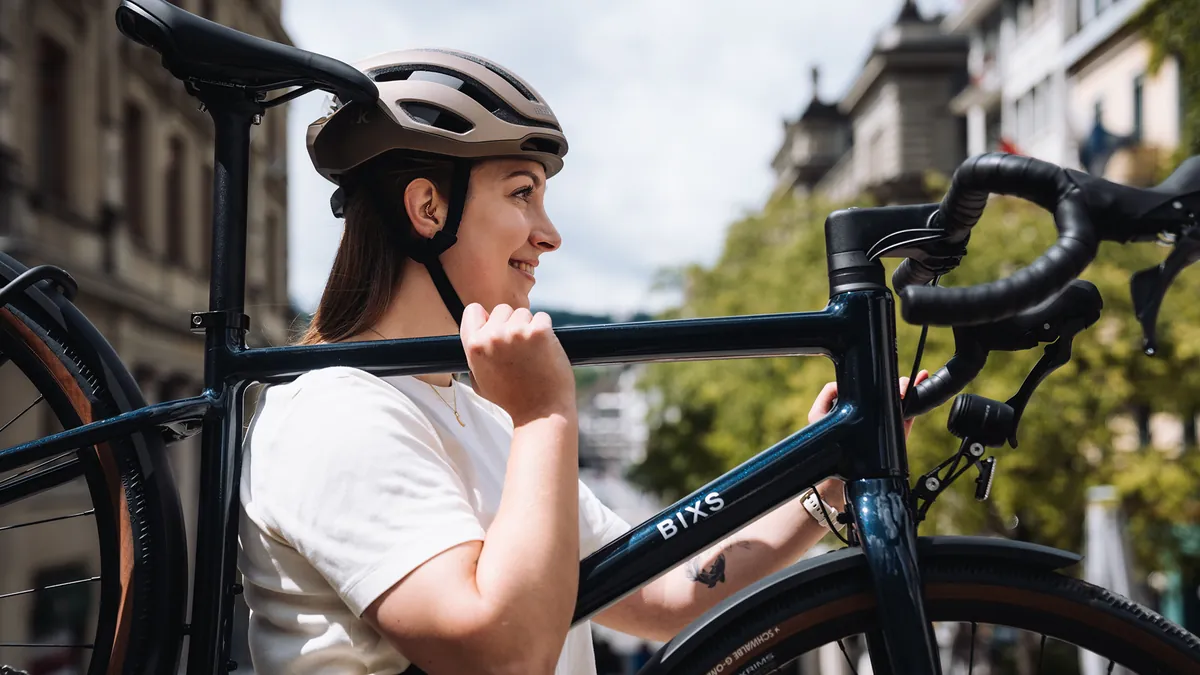 Lächelnde Fahrerin trägt ihr BIXS District Rennrad am Rahmen durch die Stadt