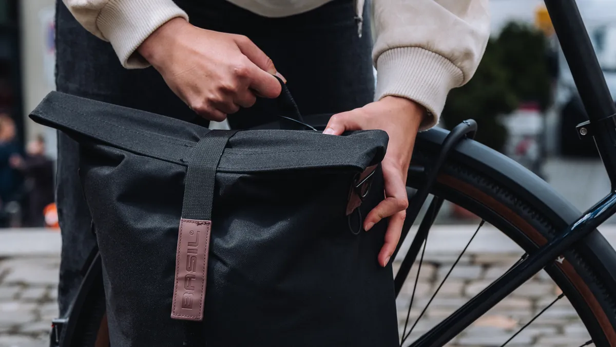 Person befestigt schwarze Basil-Gepäcktasche am Gepäckträger des BIXS District E-Bikes