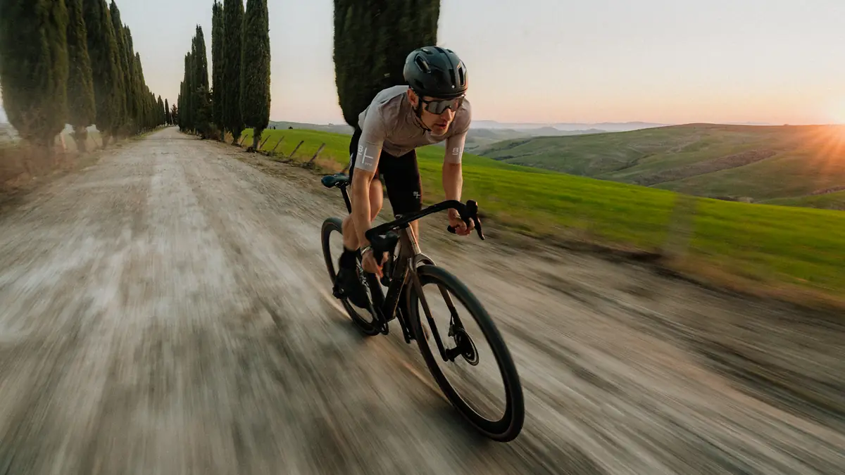 BIXS Gravel-Bike-Fahrer rast über Schotterweg zwischen Zypressen bei Sonnenuntergang