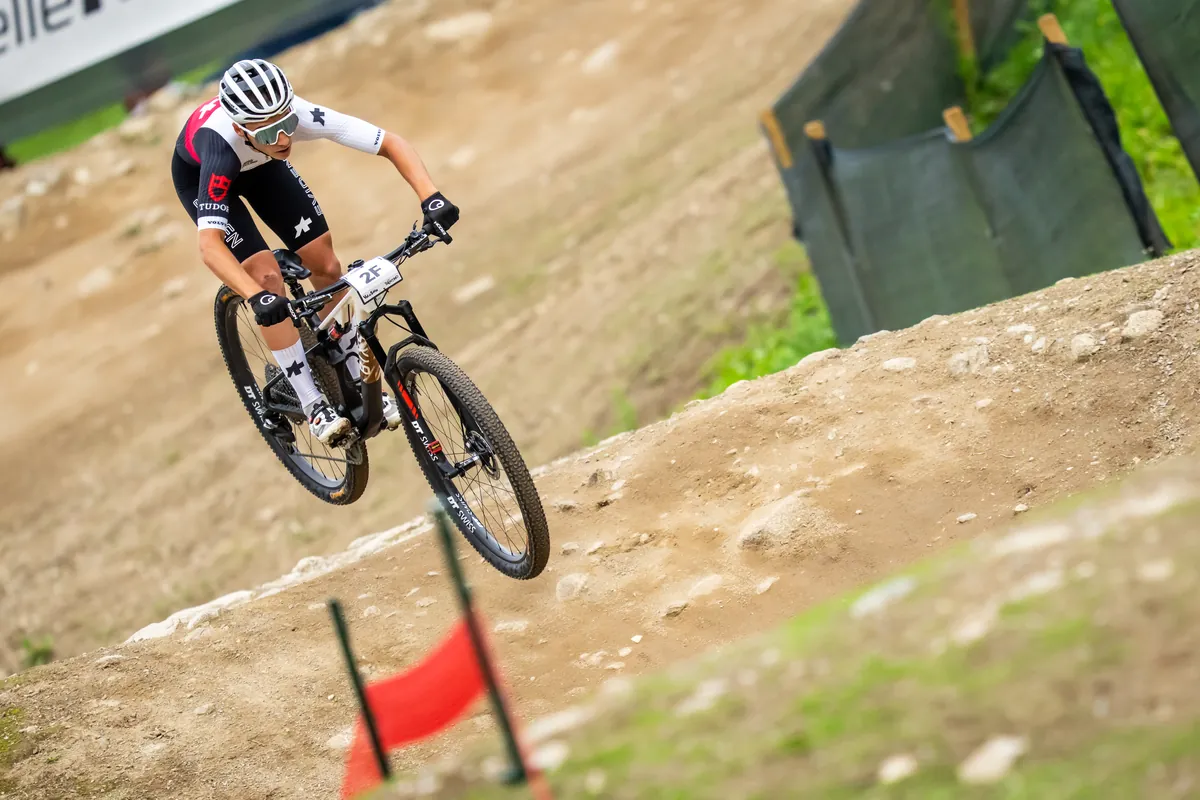 Schweizer Fahrer im SUI-Trikot auf dem BIXS Cross-Country-Bike springt über eine Kuppe des WM-Kurses