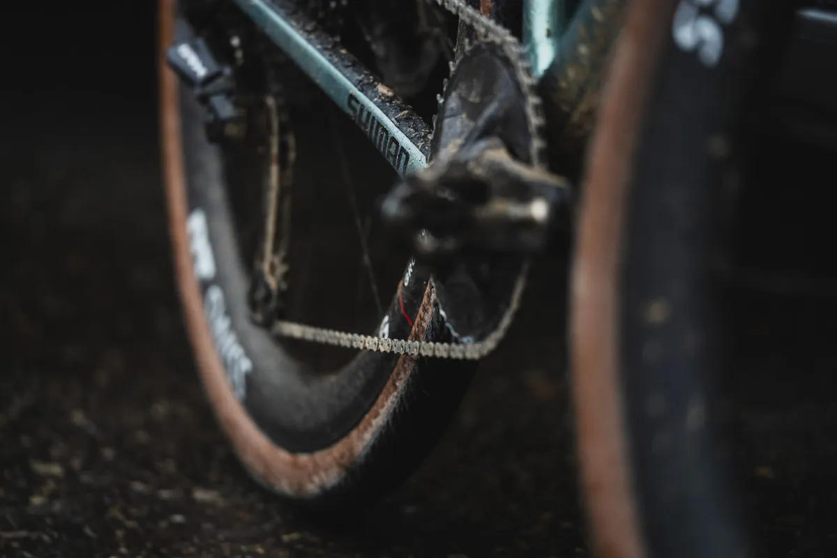 Nahaufnahme von Kurbel, Kette und Laufrädern eines verdreckten Gravelbikes, aus Bodenhöhe fotografiert