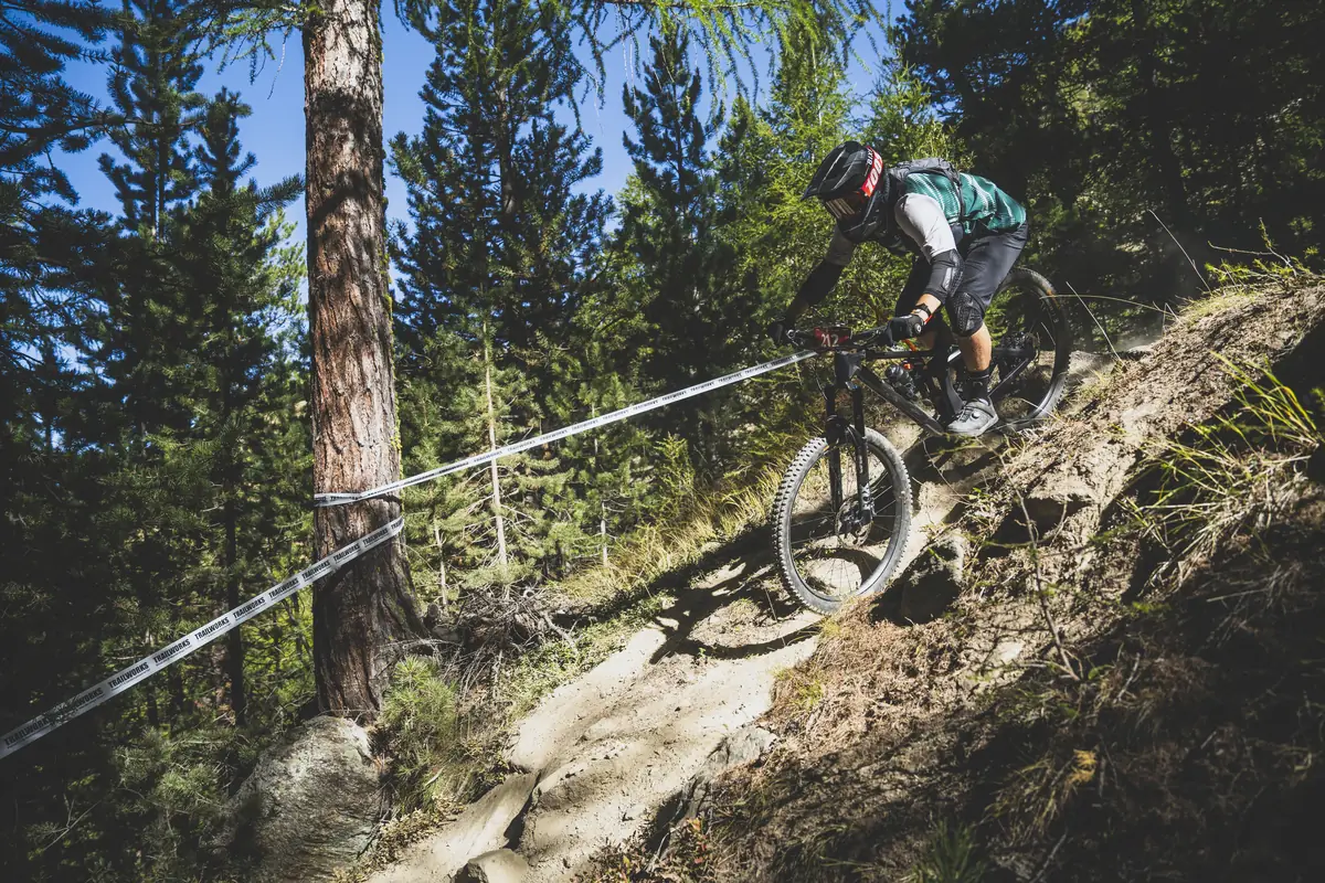 Enduro-Fahrer auf einem steilen Trail zwischen Nadelbäumen