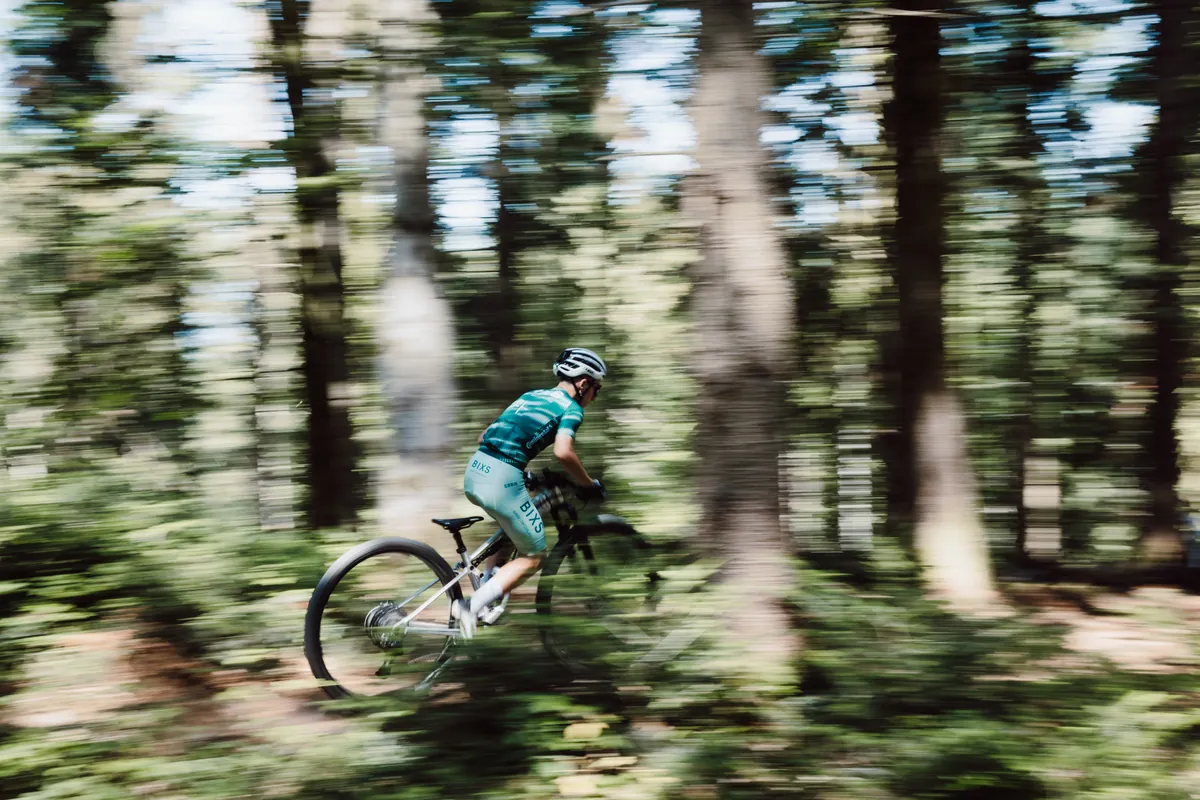 Mitzieher-Aufnahme eines Fahrers im BIXS-Trikot auf dem Prototyp, der Wald verwischt vollständig