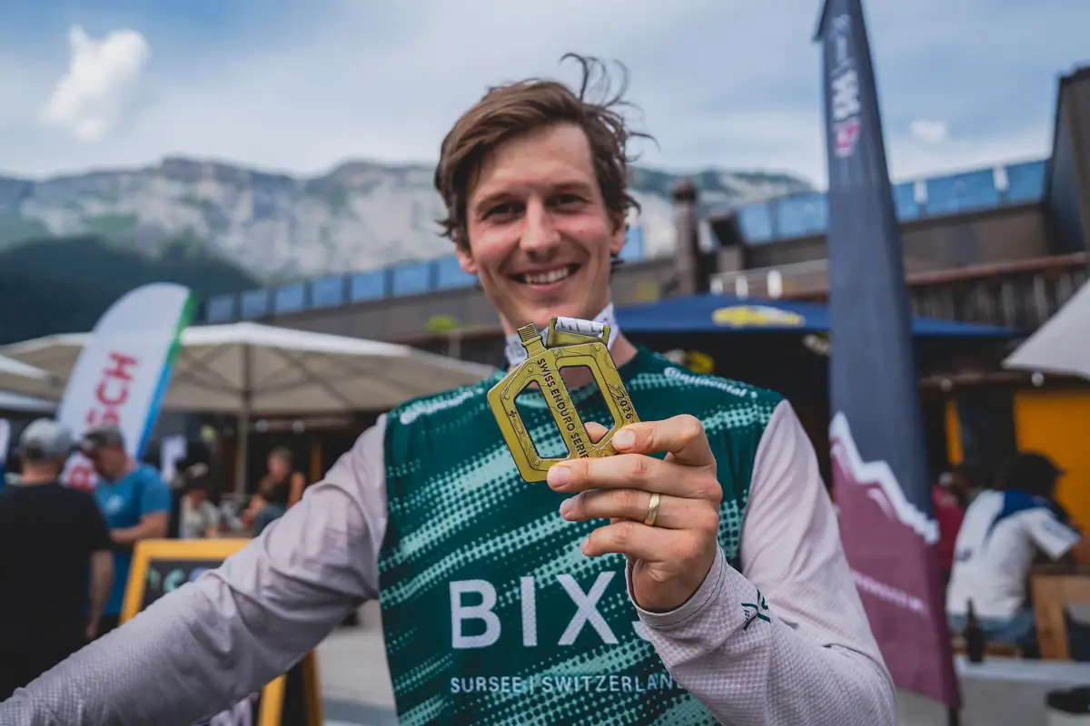BIXS Rennfahrer präsentiert Pedal-Trophäe der Swiss Enduro Series vor Bergpanorama