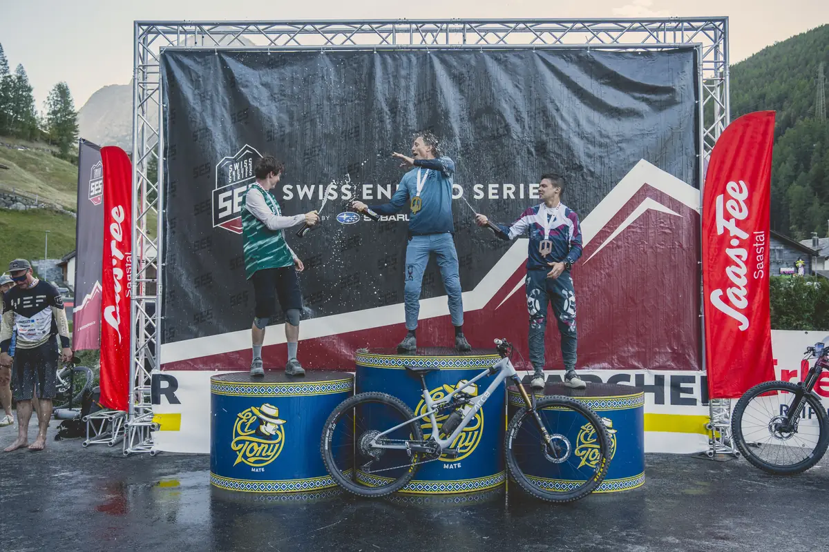 Drei Fahrer spritzen sich auf dem Podest der Swiss Enduro Series mit Sekt ab, links ein Fahrer im BIXS Trikot.