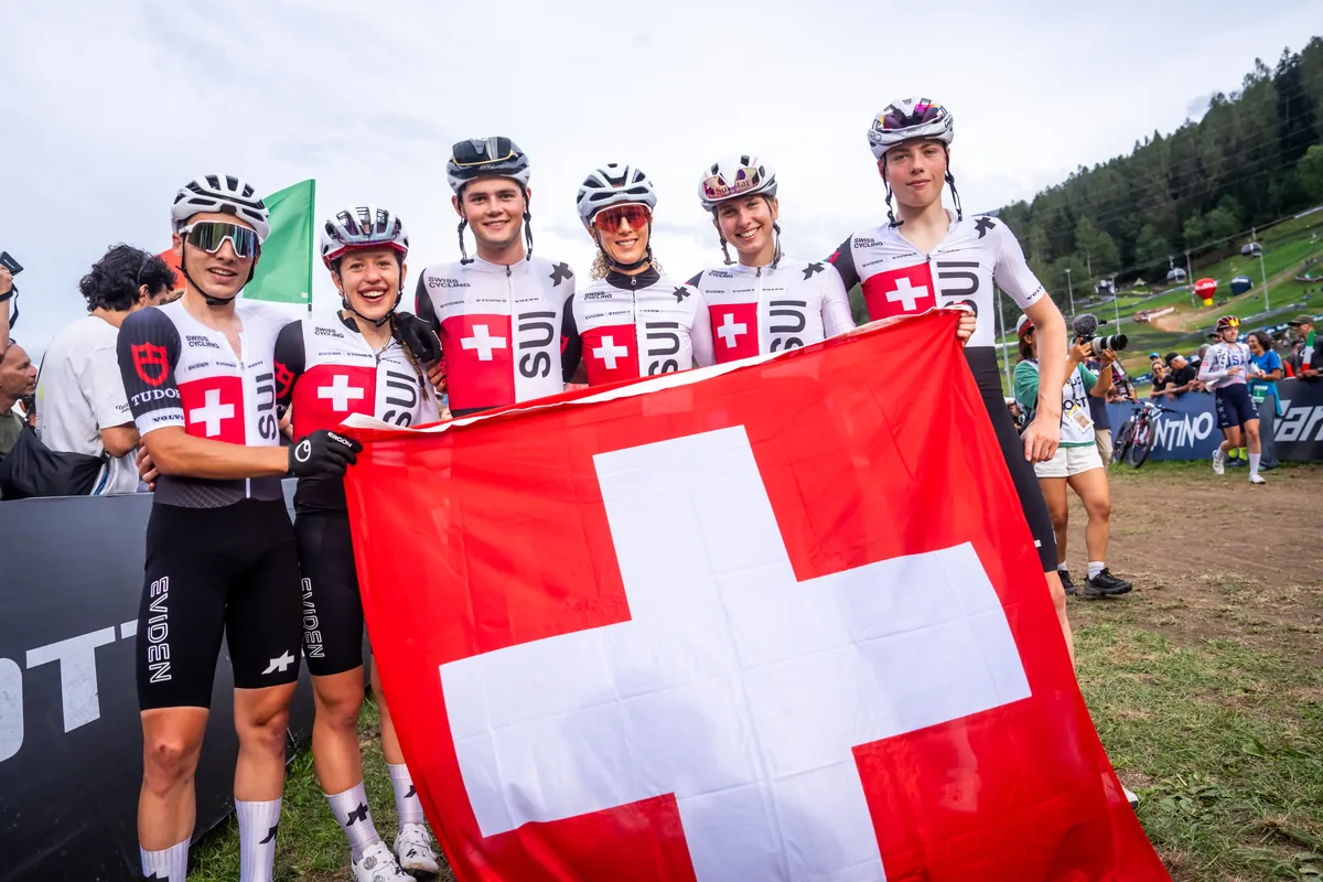 Sechs Fahrerinnen und Fahrer des Schweizer Teams halten im Zielbereich gemeinsam eine Schweizer Fahne