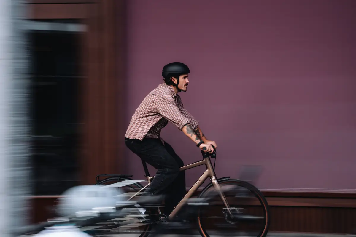 Mann fährt District-Bike durch urbane Strasse vor pinker Fassade, Bewegungsunschärfe