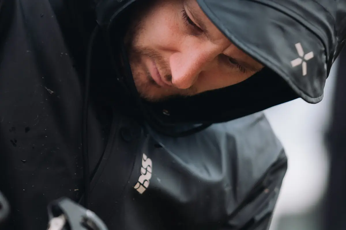Nahaufnahme eines Mannes mit Kapuze und IXS-Regenjacke, lächelnd nach unten blickend