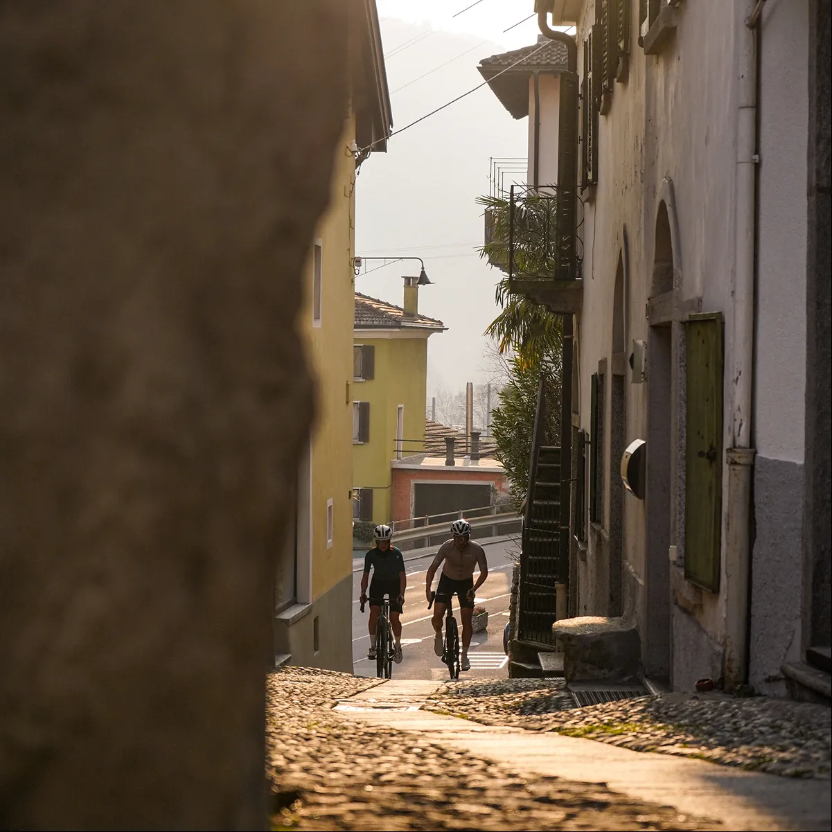 Zwei Rennradfahrer fahren eine steile Gasse in einem italienischen Dorf hinauf
