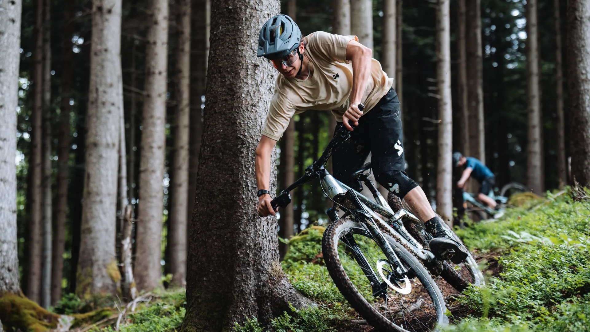 E-Mountainbiker fährt dynamisch um einen Baum auf einem Waldtrail