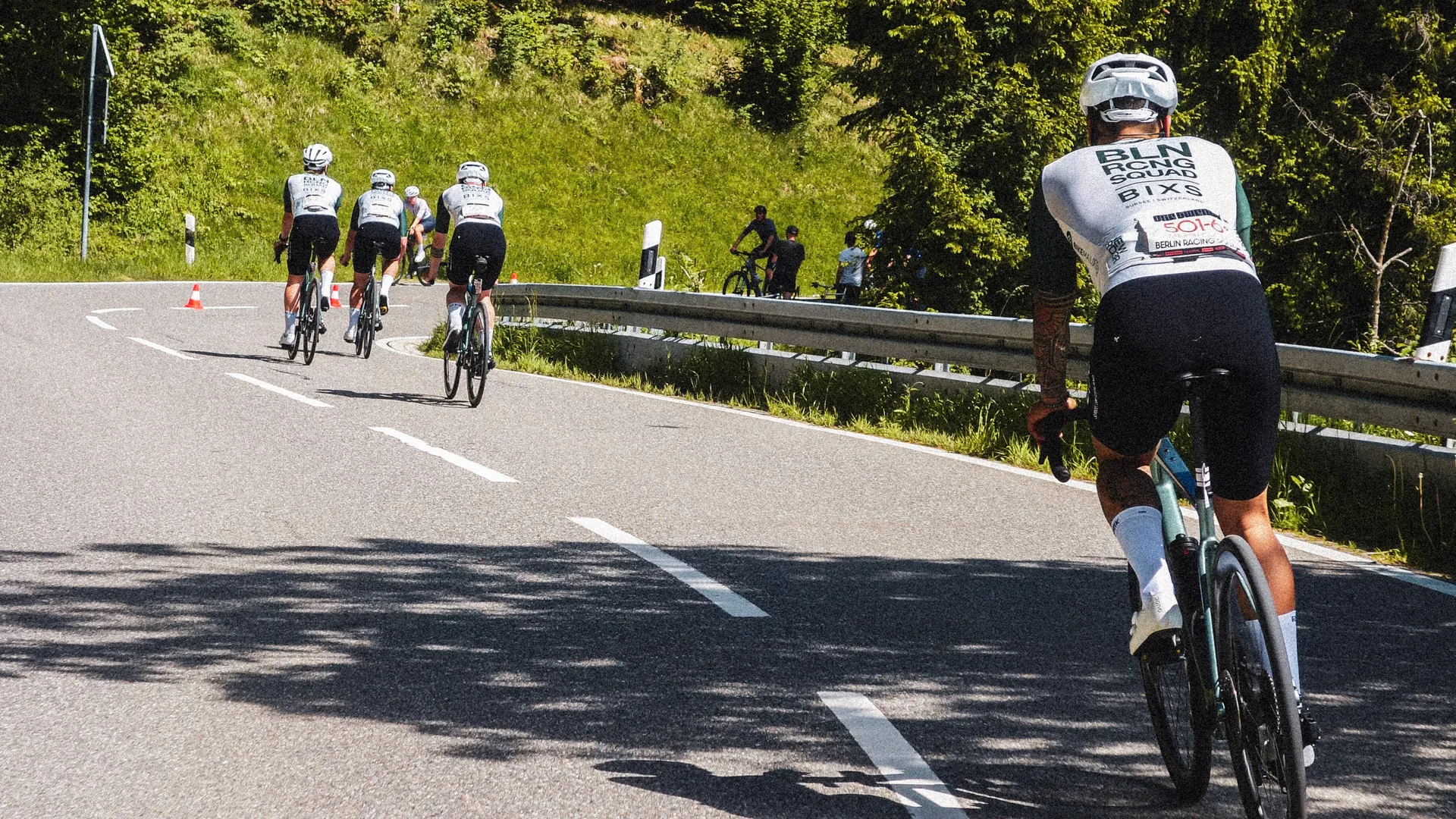 Rennradfahrer-Gruppe im Renntrikot auf kurvenreicher Bergstrasse von hinten