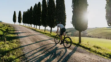 Fahrer mit BIXS Gran Turismo GR Gravelbike auf Schotterweg zwischen toskanischen Zypressen