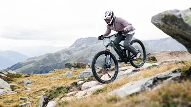 Fahrer mit Vollvisierhelm im technischen Downhill-Trail zwischen Felsen im Hochgebirge