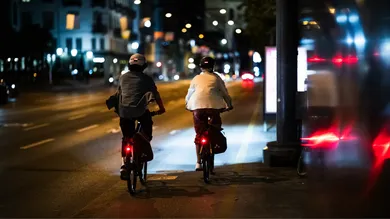 Zwei Fahrer:innen mit Gepäcktaschen und Rücklicht bei Nacht auf Radweg, Rückansicht