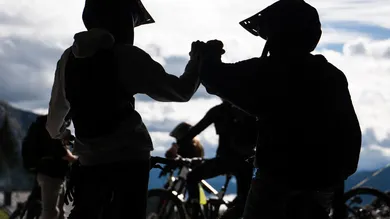 Zwei Mountainbiker geben sich im Gegenlicht einen Fist-Bump vor Wolkenhimmel
