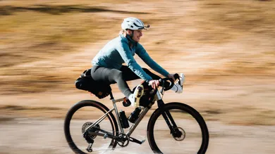 Fahrerin mit BIXS Traverse Gravelbike in dynamischer Fahrt durch flaches Wasser