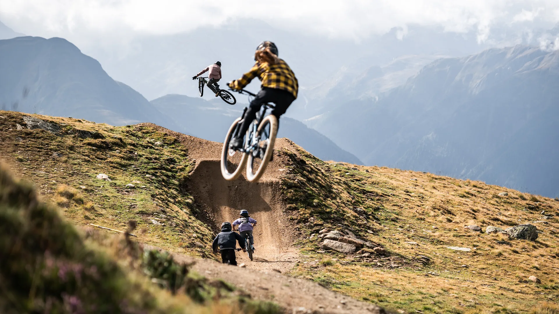 Jugendliche springen mit Mountainbikes über einen Dirt-Kicker in den Alpen