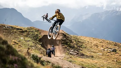 Jugendliche springen mit Mountainbikes über einen Dirt-Kicker in den Alpen