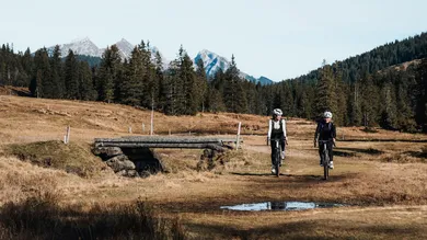 Zwei Fahrerinnen mit BIXS Traverse Gravelbikes auf Alpwiese vor Bergpanorama
