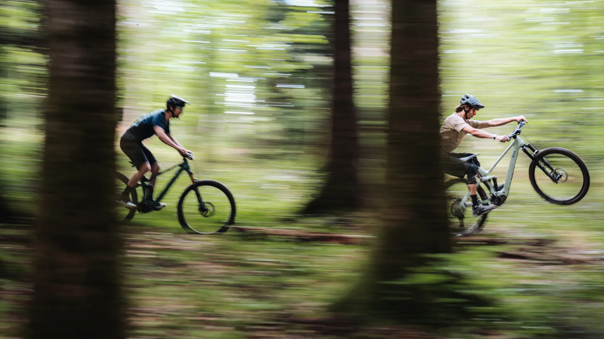 Zwei Mountainbiker fahren mit hohem Tempo durch einen sonnendurchfluteten Wald