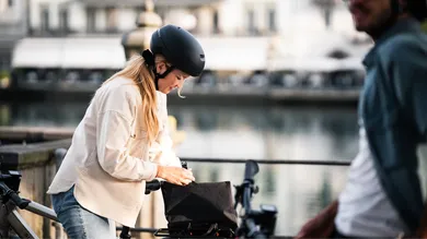 Fahrerin öffnet Gepäcktasche am Rahmen ihres E-Bikes vor Kanalkulisse in der Altstadt