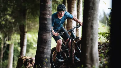 Fahrer mit erdverschmiertem Trail-Bike zwischen Baumstämmen im Wald