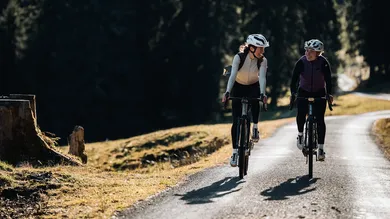Zwei lachende Fahrerinnen auf BIXS Gravelbikes auf einer Bergstrasse im Herbstlicht