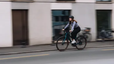 BIXS District E-Bike, Frau fährt durch die Stadt an einer Häuserfassade vorbei